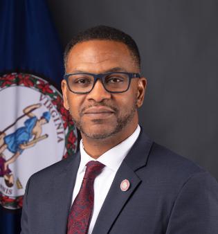 Marcus Thornton, Deputy Chief Data Officers, wears a suit in his headshot and sits in front of the Virginia Flag